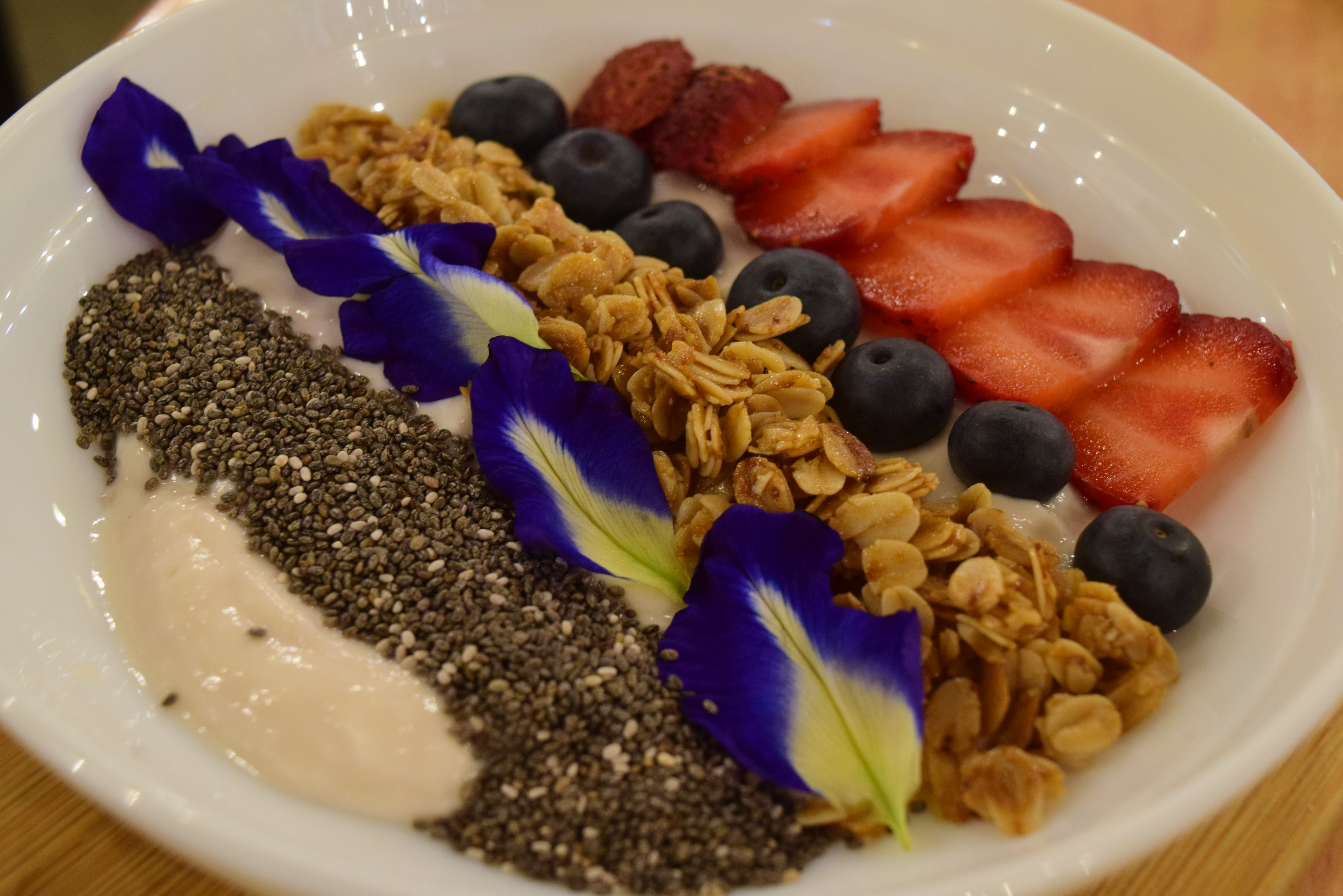 Consists of strawberry yogurt, granola, chia seeds, strawberries, blueberries, and blue ternates