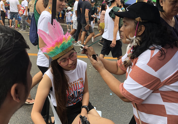 シヌログのTシャツを着て髪飾りを付けた女の子が、顔に模様を描いてもらっています。本当にお祭り期間の「何でもあり！」という自由奔放な雰囲気がシヌログの一つの魅力とも言えます。